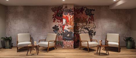 A room with a large graffiti wall, two white armchairs, a small wooden table, and potted plants.