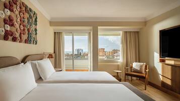 A hotel room with two beds, a large window, a television, and a city view.