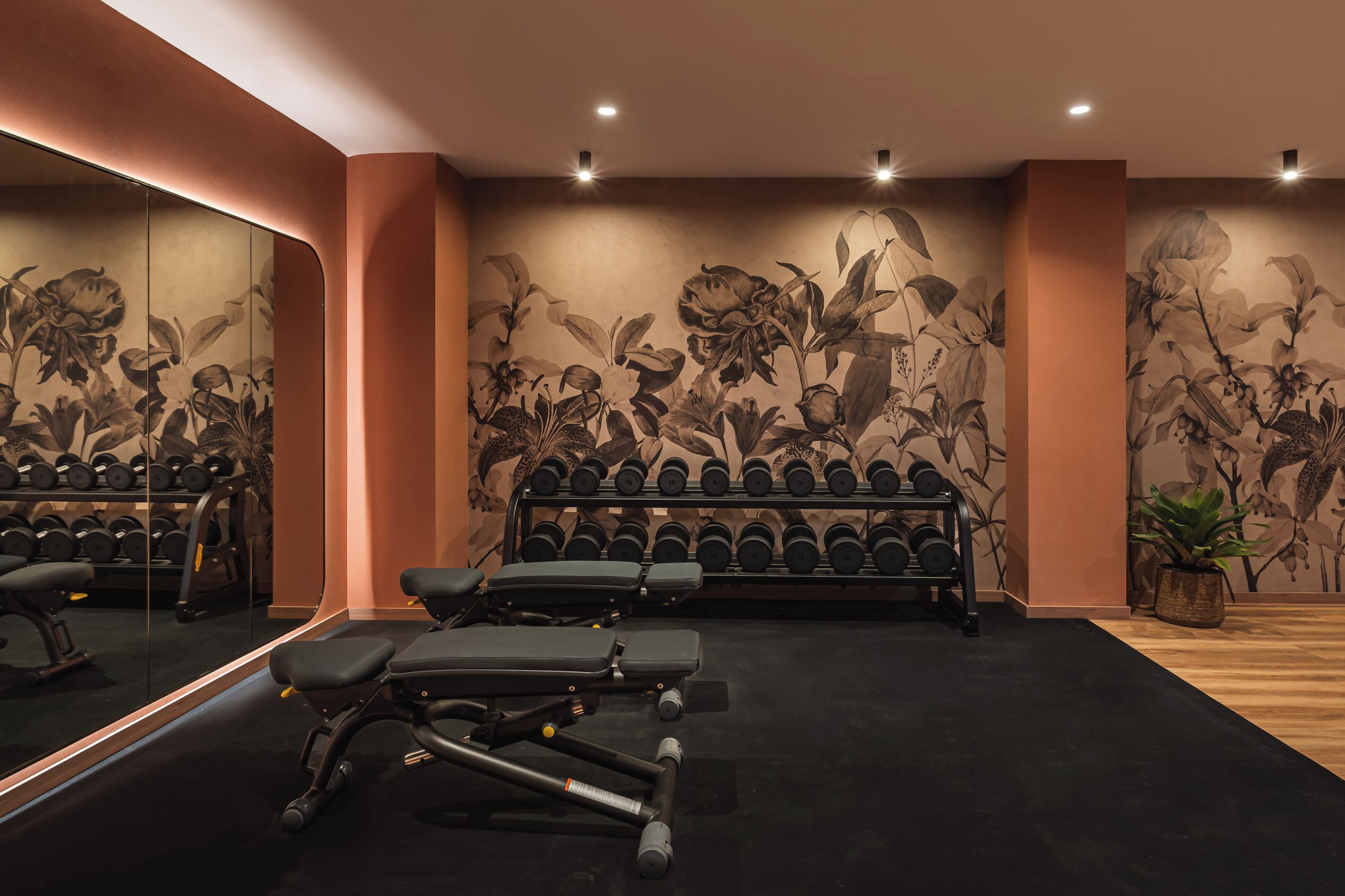 A gym with exercise equipment, a mirrored wall, and a floral mural.