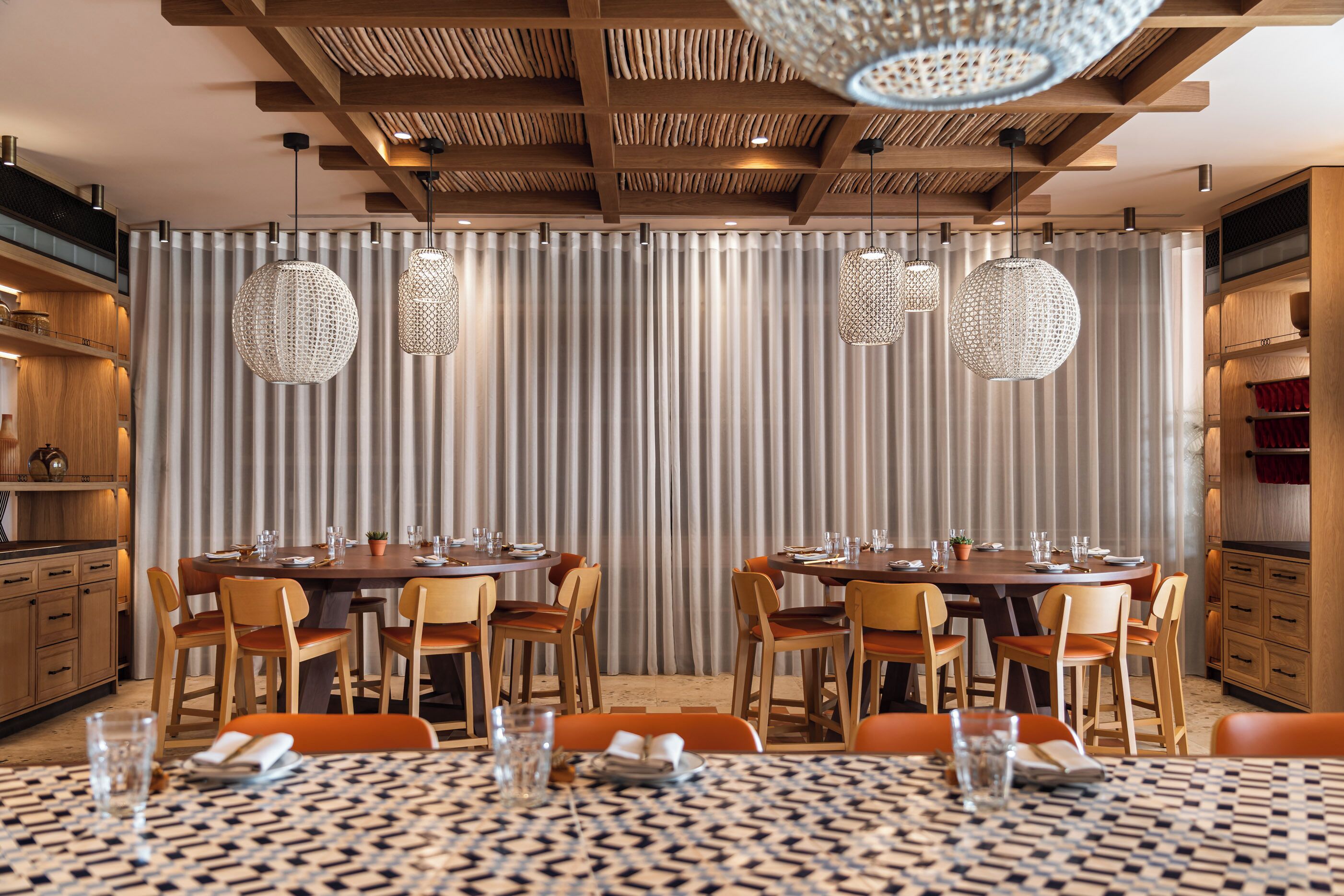 Un espace de restauration moderne avec deux tables rondes, des chaises en bois et des luminaires sphériques suspendus.