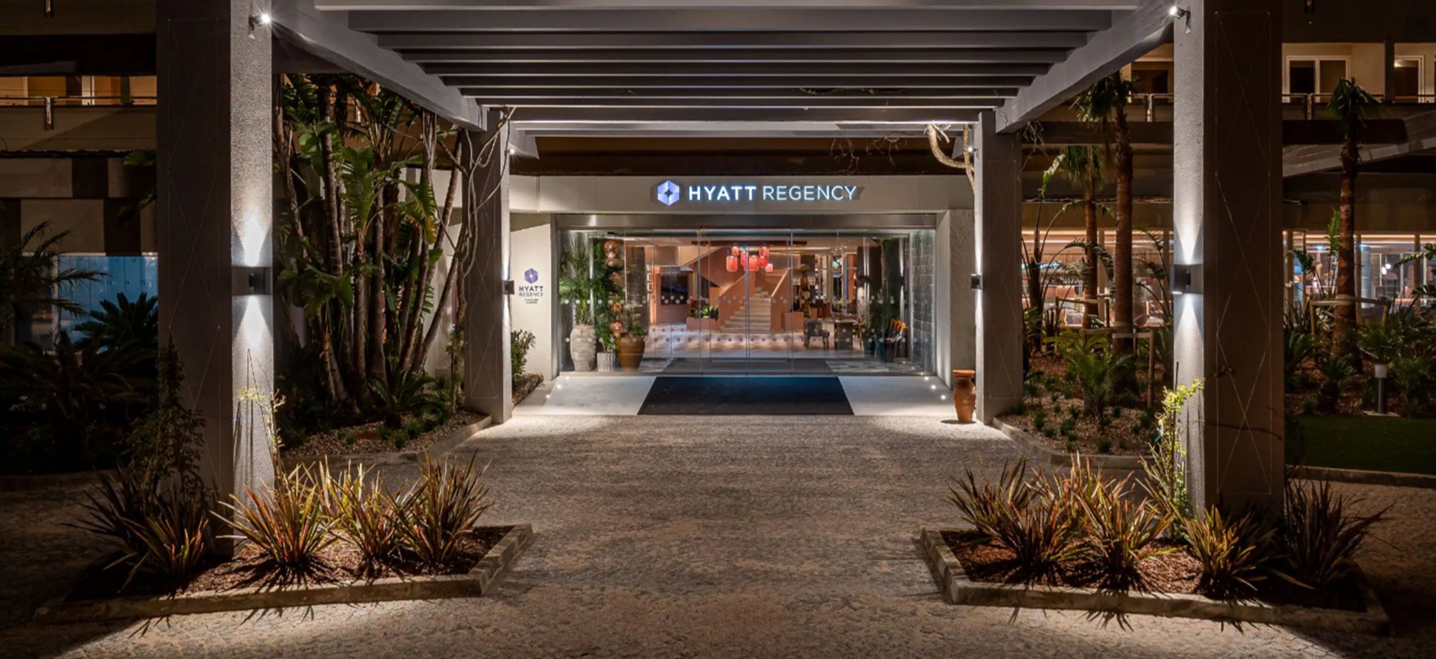 A Hyatt Regency hotel entrance with a covered walkway, indoor plants, and a sign above the entrance.