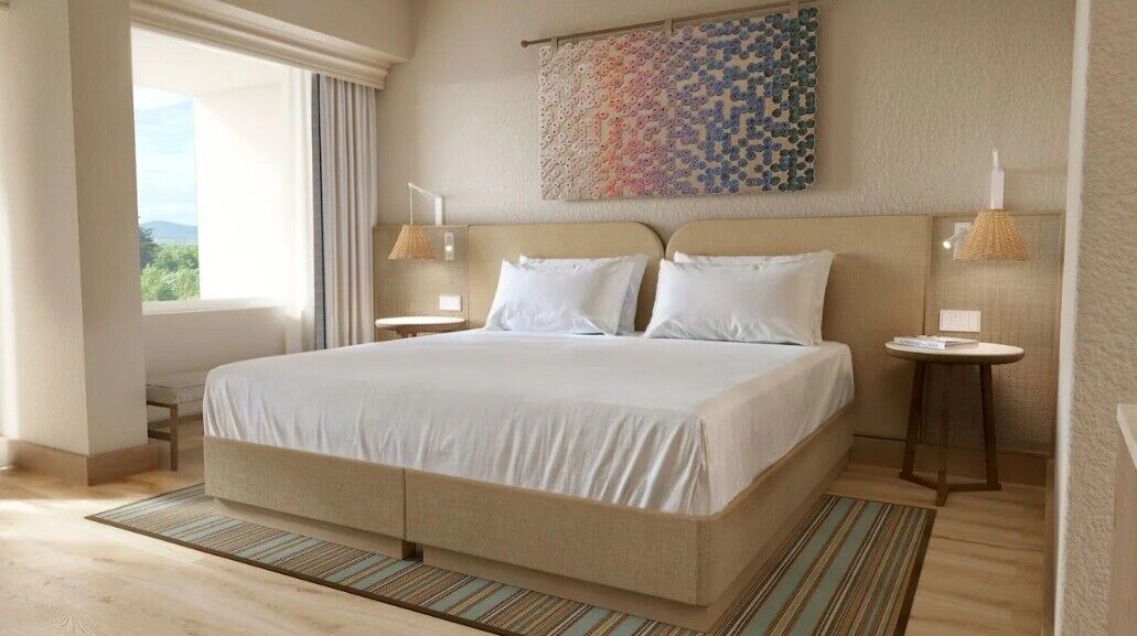 Ein Hotelzimmer mit einem großen Bett, zwei Nachttischen, einem mit Vorhängen versehenen Fenster, einem an der Wand hängenden Kunstwerk und einem Holzboden.