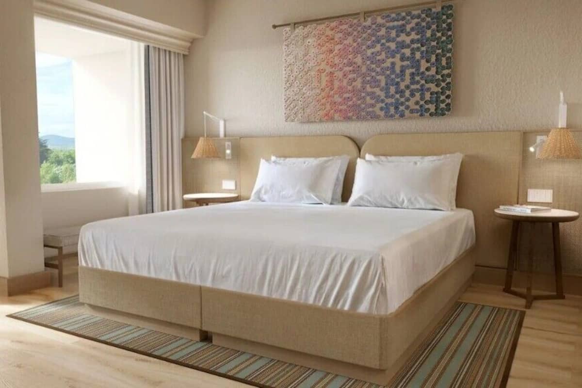 Una habitación de hotel con una cama grande, dos mesitas de noche, un ventanal con cortinas, una obra de arte colgada en la pared y suelo de madera.