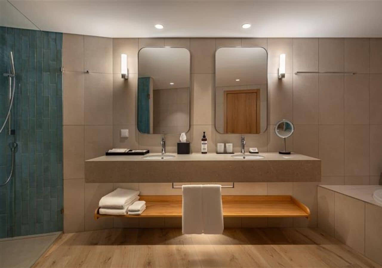 Un baño moderno con lavamanos doble, dos espejos, toallero y zona de ducha.