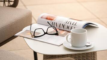 A wicker chair, a white table with a magazine, a pair of glasses, and a white mug.