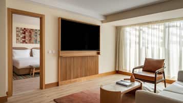 A hotel room with a bed, a TV, a sofa, a coffee table, and a window with curtains.