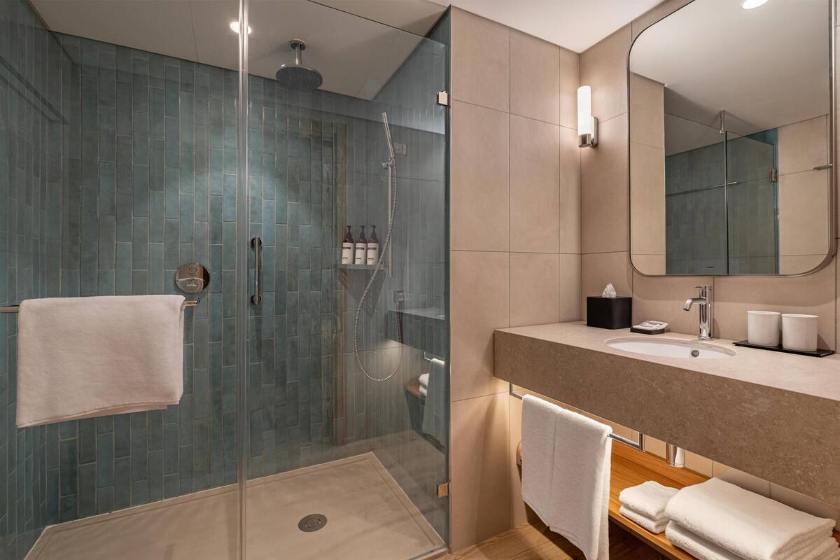 A modern bathroom with a glass-enclosed shower, a sink with a mirror, and neatly arranged towels.