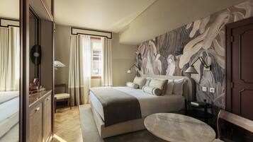 Una habitación de hotel con una cama grande, una mesa redonda, un escritorio con una lámpara y una pared con estampado floral.