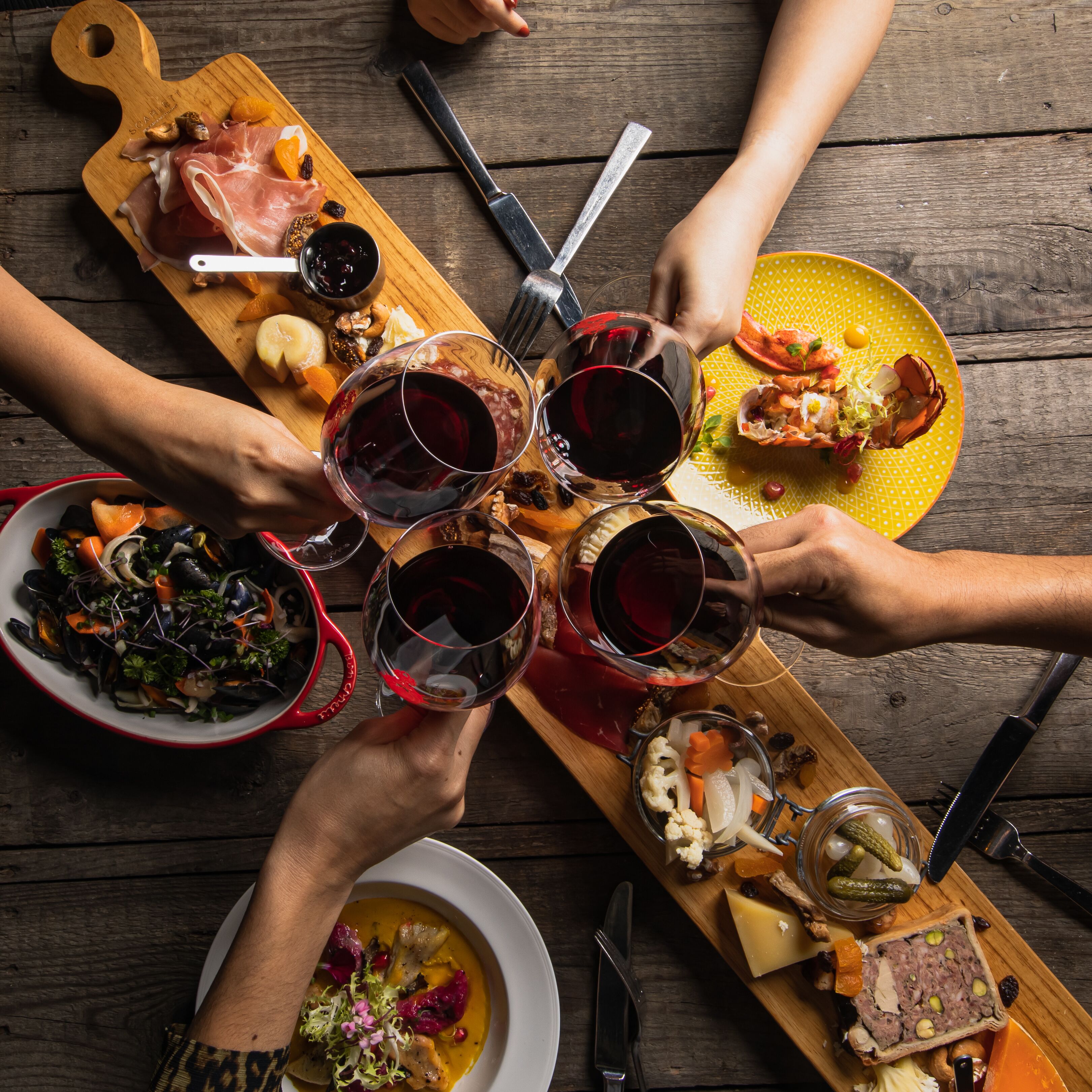 A group of people around a wooden table with various food items and wine glasses.