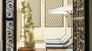 Un patio con una reja metálica decorativa, sillas de descanso y plantas en macetas.