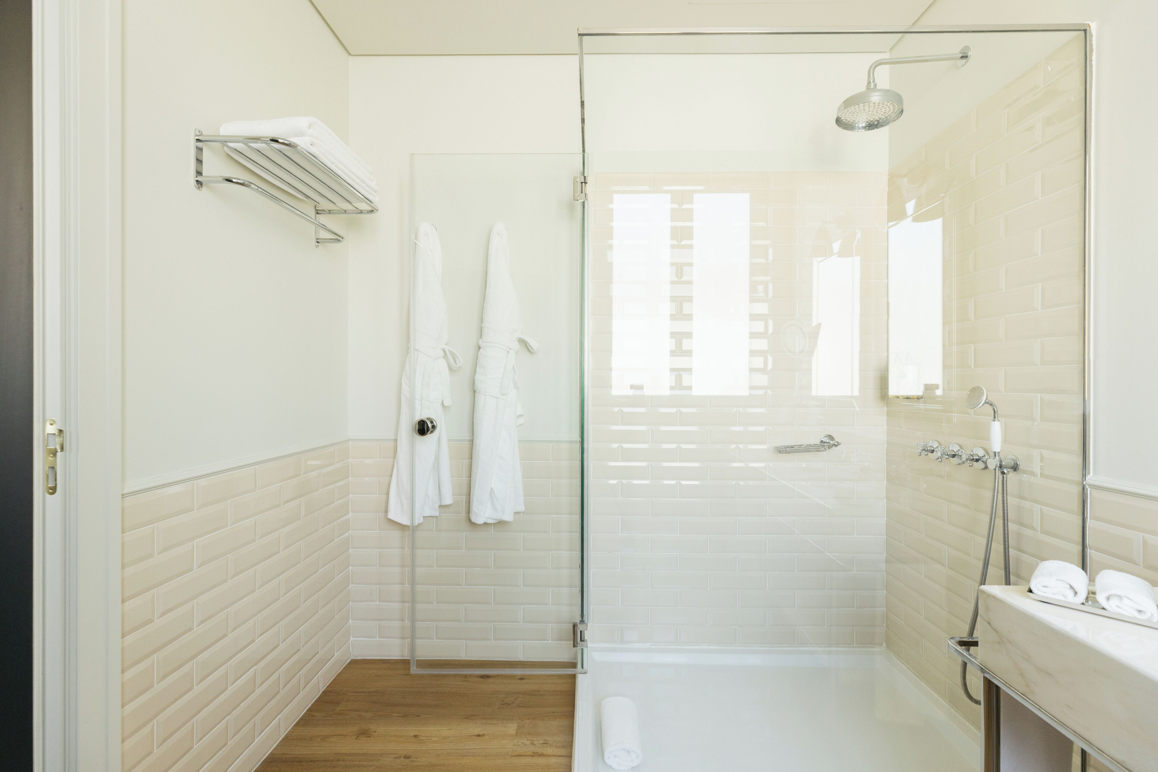 Een moderne badkamer met een douchecabine van glas, een witte betegelde muur en een houten vloer.