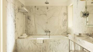 A modern bathroom with a marble wall, a freestanding bathtub, a glass-enclosed shower, and a vanity with a mirror.