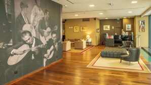 A lobby with wooden flooring, a large wall mural, a sofa, a chair, and a reception desk. - VIP Executive Saldanha Hotel (Lisbon)