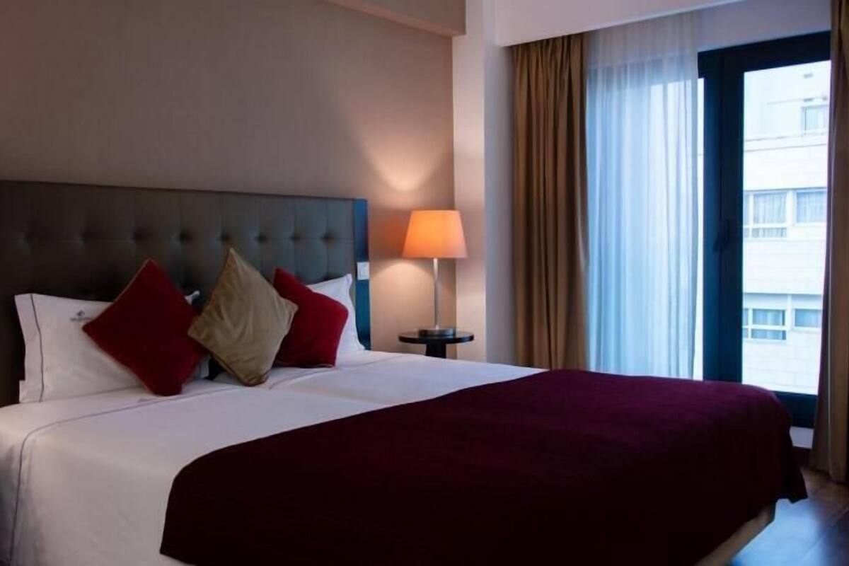 Una camera d'albergo con un letto grande, un comodino, una lampada e vista all'esterno da una finestra.