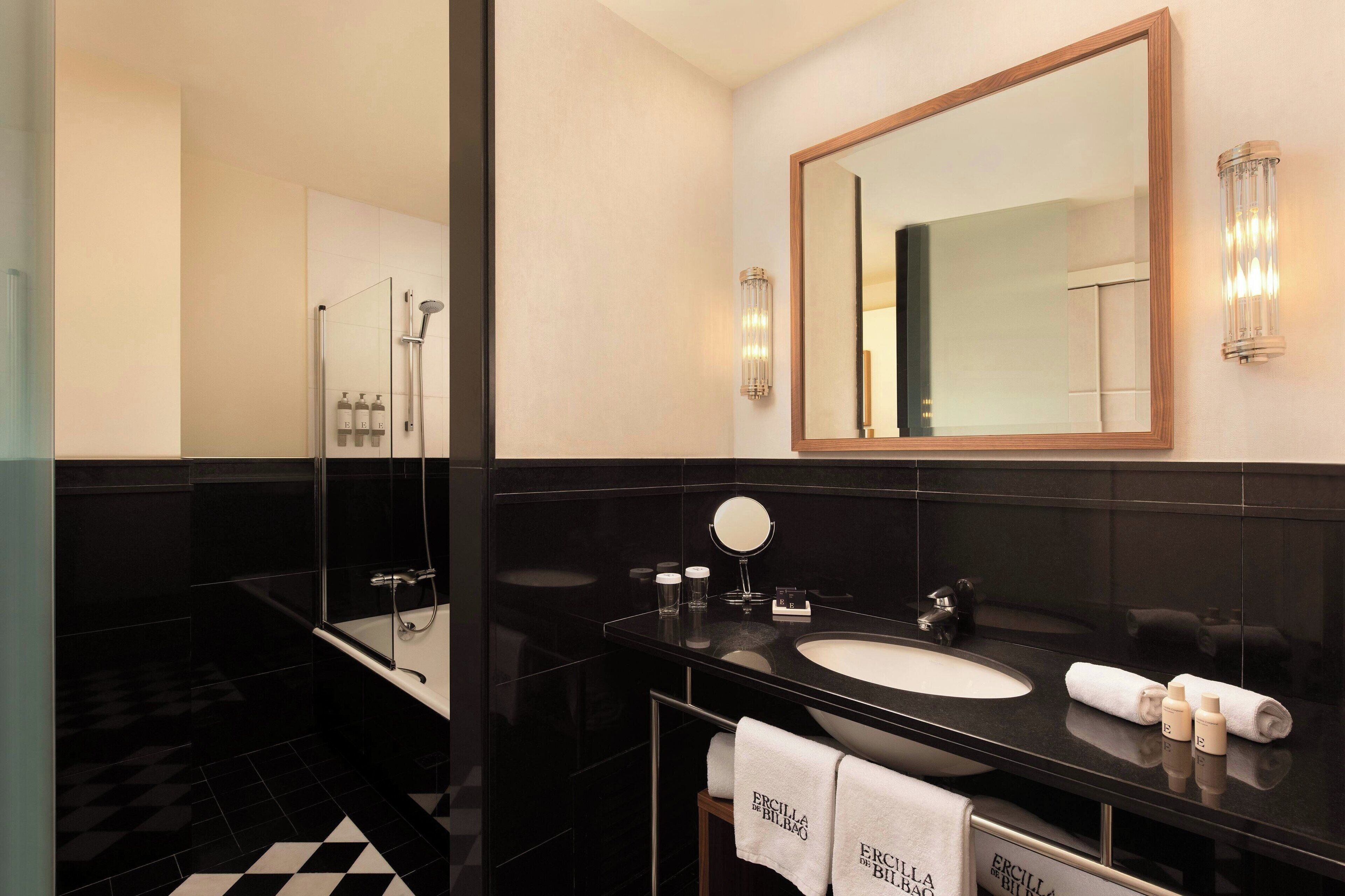 Un baño moderno con piso a cuadros blanco y negro, un espejo grande, un lavamanos y una ducha.