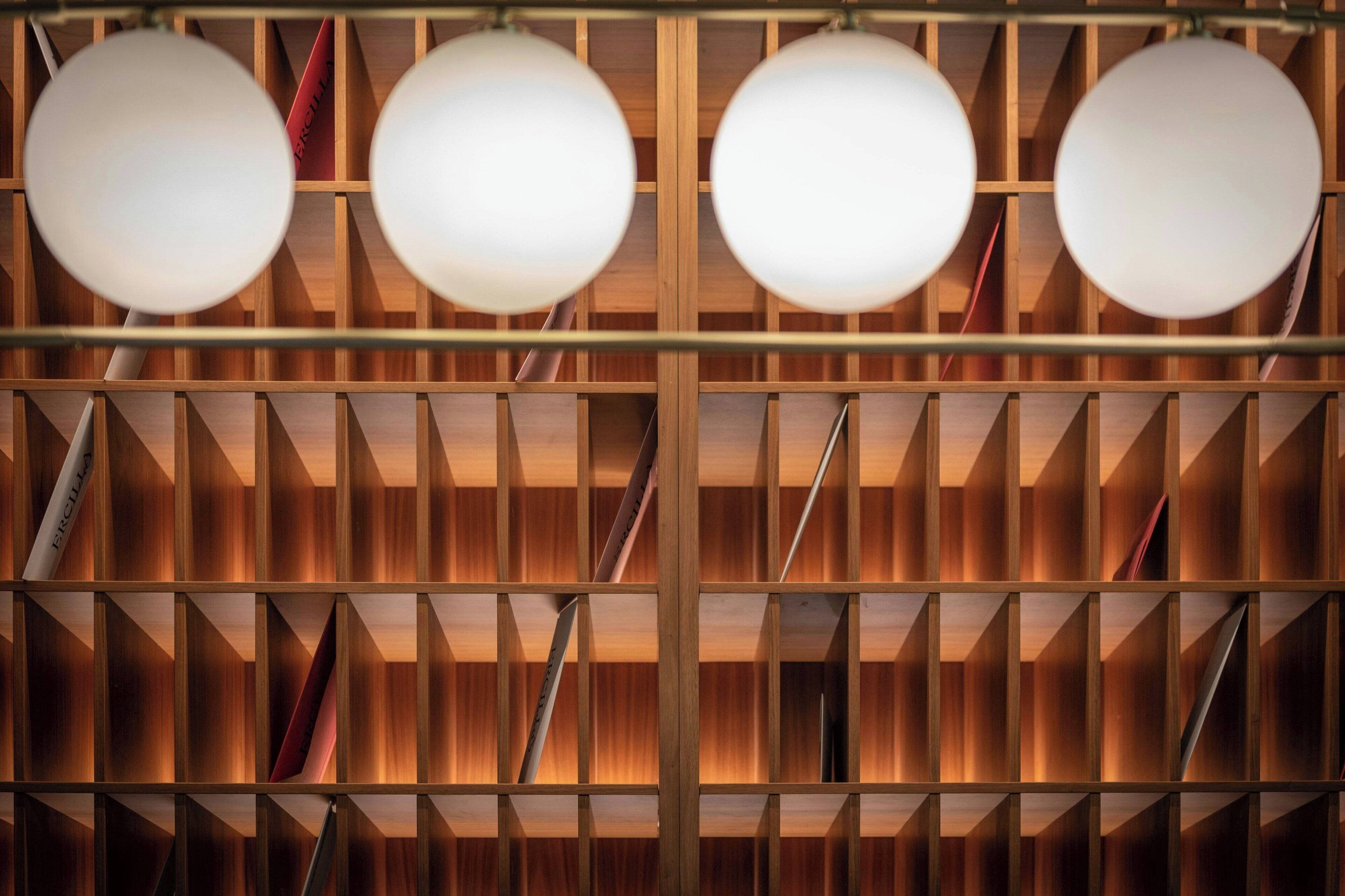 A wooden bookshelf with multiple levels and shelves, illuminated by round ceiling lights.