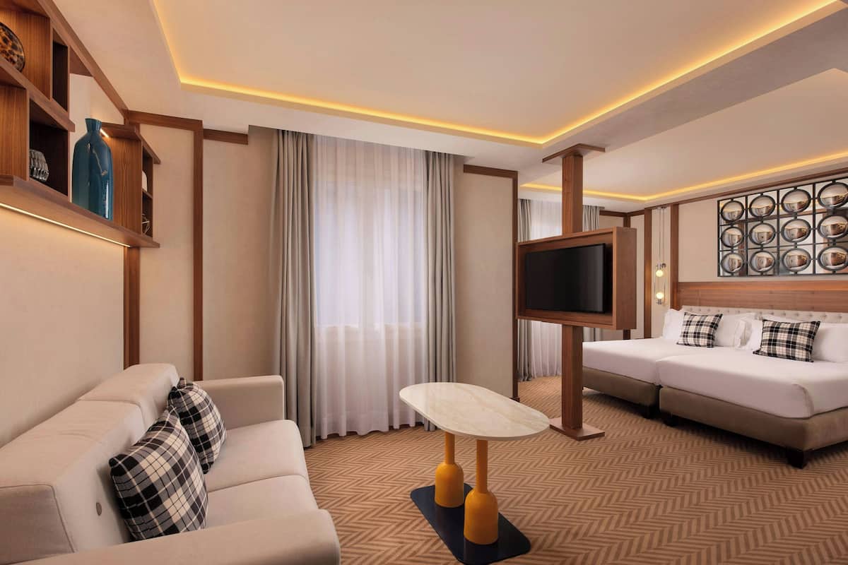 Ein modernes Hotelzimmer mit einer Couch, einem Bett, einem Fernseher und einem Tisch mit einer Lampe.