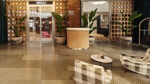 Un hall d’entrée avec un sol à carreaux, un pilier central en bois et deux plantes en pot.