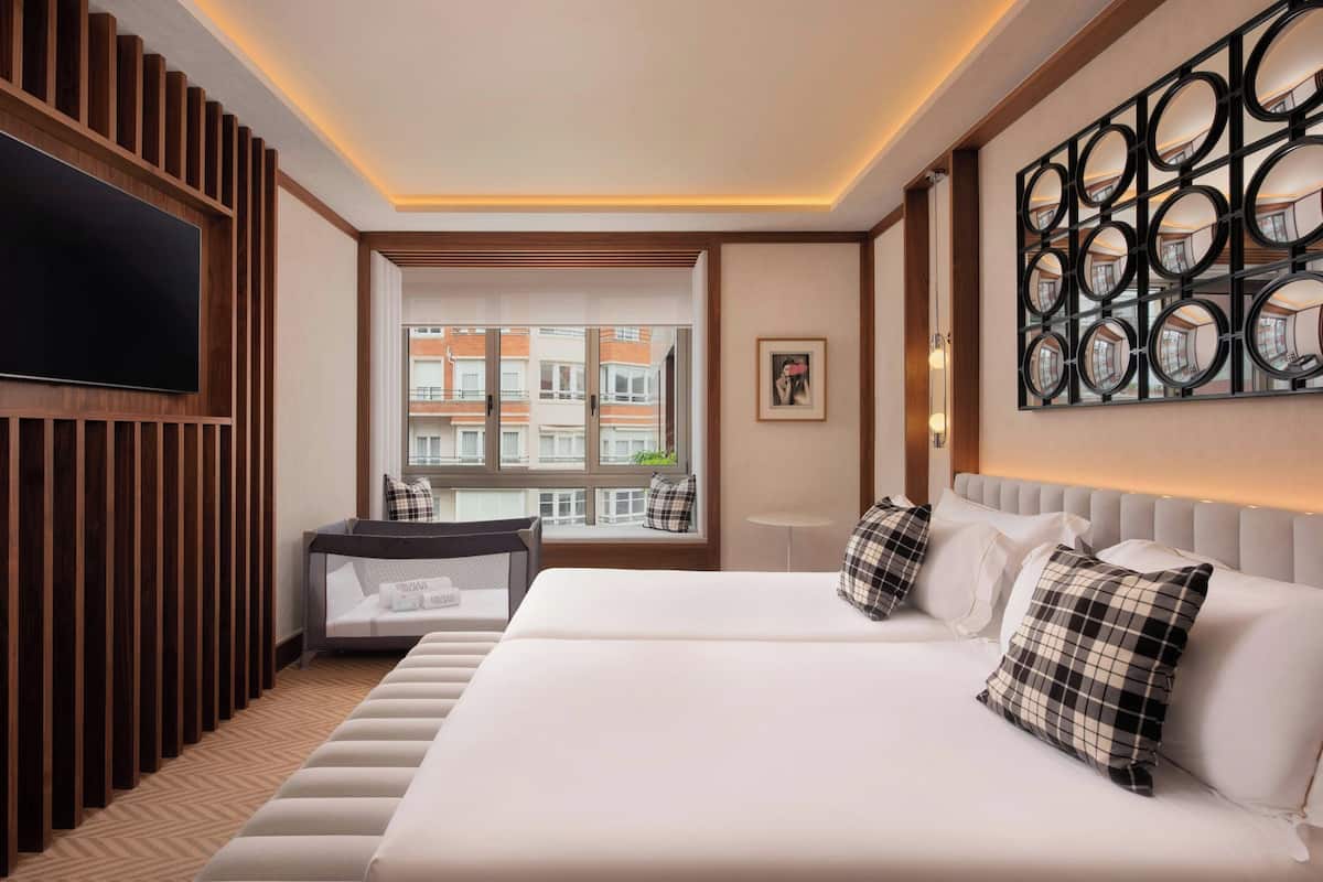 Ein Hotelzimmer mit einem großen Bett, einer Couch, einem Fernseher und einem Fenster mit Blick auf Gebäude.