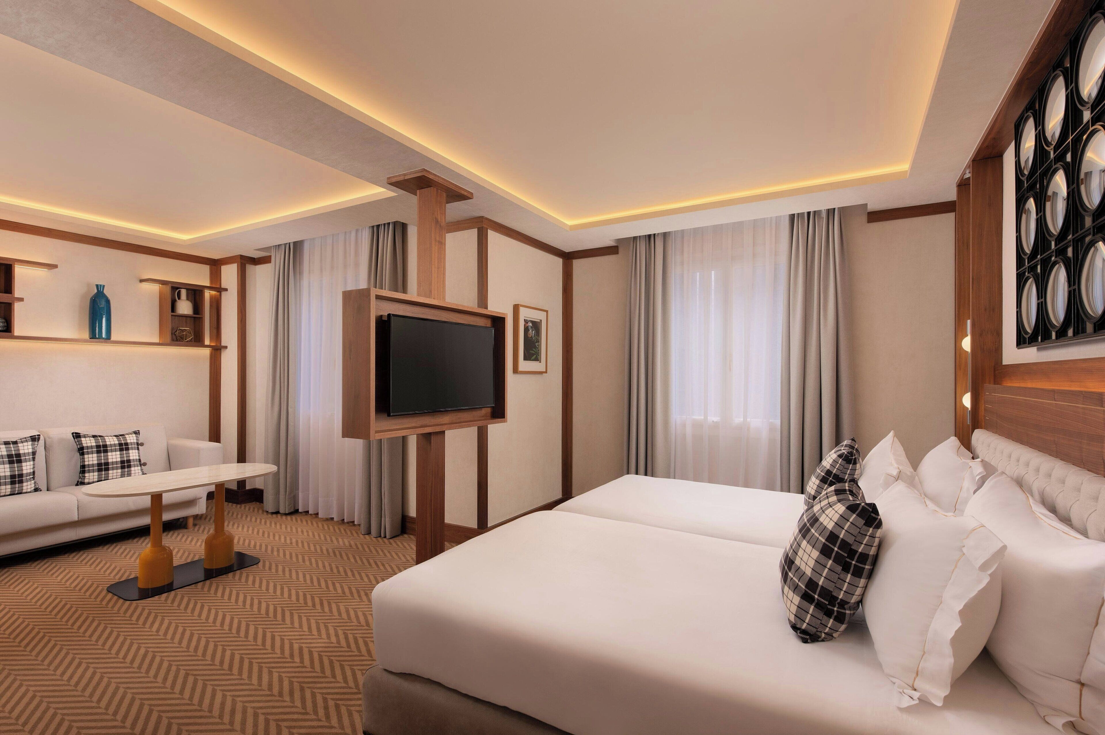 Une chambre d’hôtel comprenant un lit, un téléviseur posé sur un meuble, un canapé, une petite table et un élément décoratif mural.
