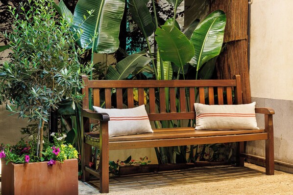 A wooden bench with two pillows, surrounded by lush greenery and potted plants. - Hotel Bonanova Park (Barcelona)