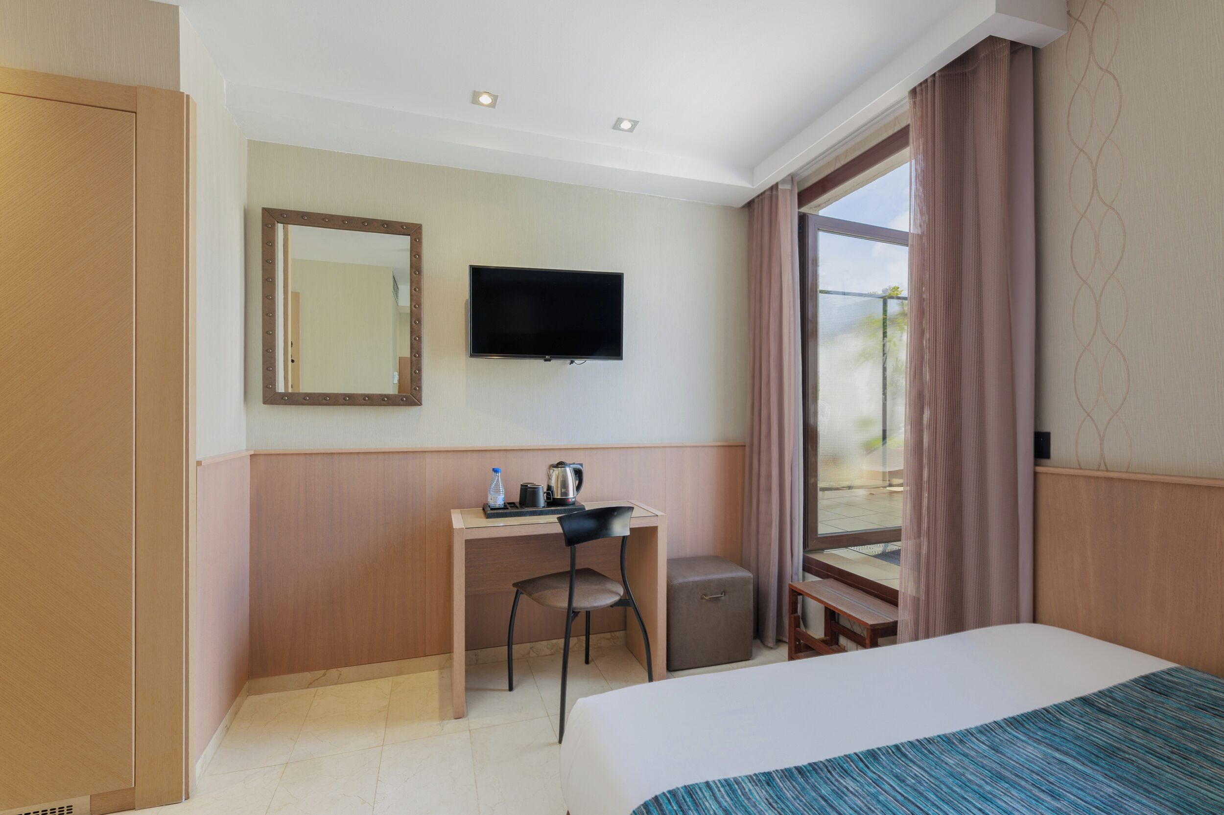 Habitación de hotel con cama, escritorio, silla, televisión y ventana con cortinas.