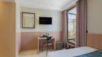 Habitación de hotel con cama, escritorio, silla, televisión y ventana con cortinas.