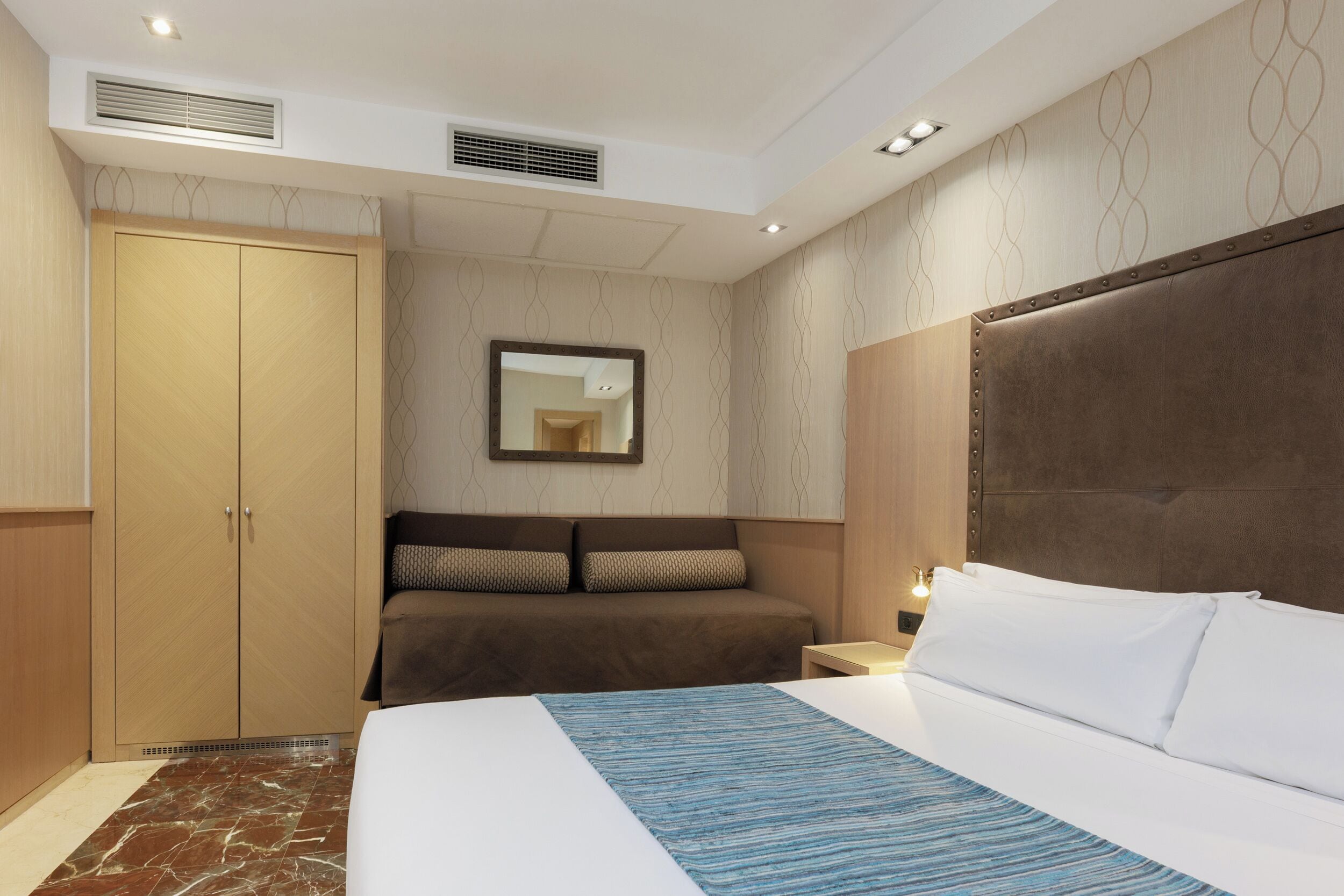 Una habitación de hotel con una cama grande, un armario, un espejo y una mesita de noche.