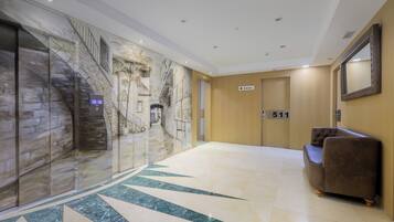 Un vestíbulo de hotel con piso de mármol, un mostrador de recepción, un sofá marrón y un mural en la pared.
