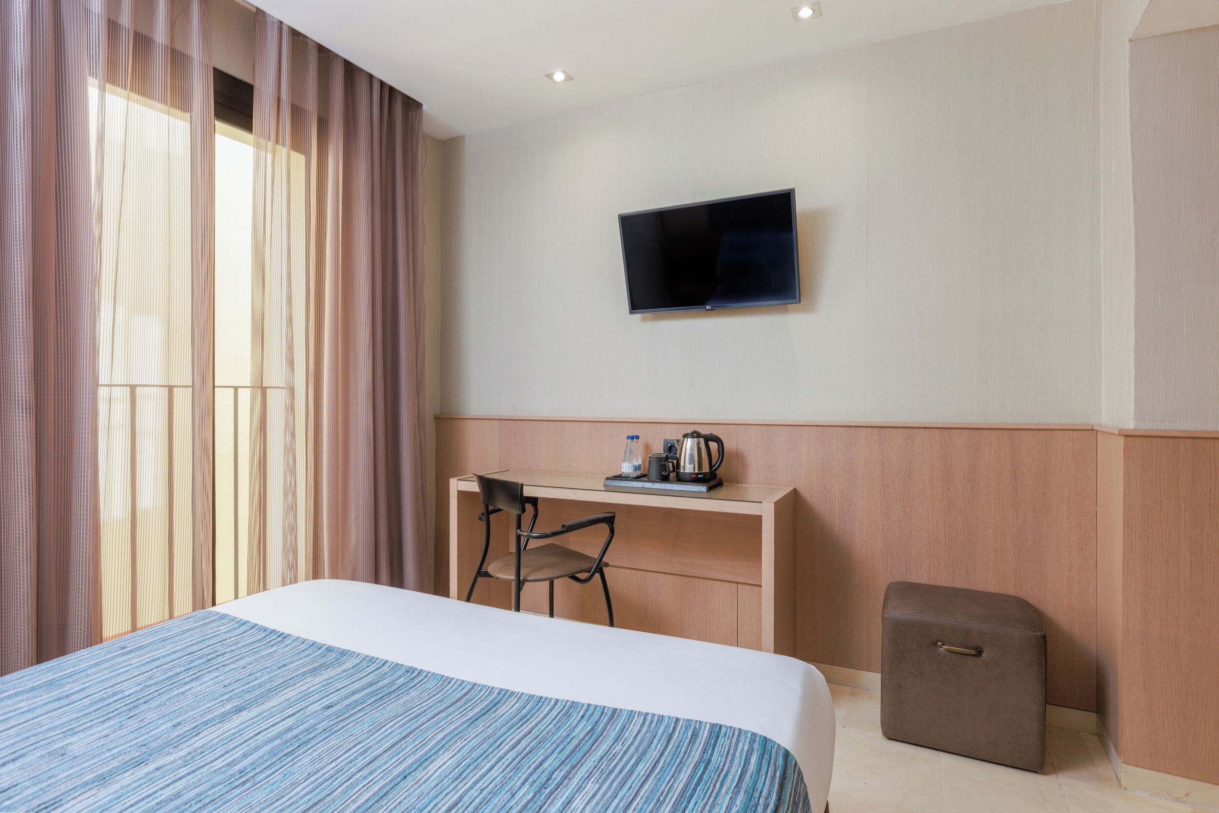 Una habitación de hotel con cama, escritorio, silla, televisor y un mueble pequeño.
