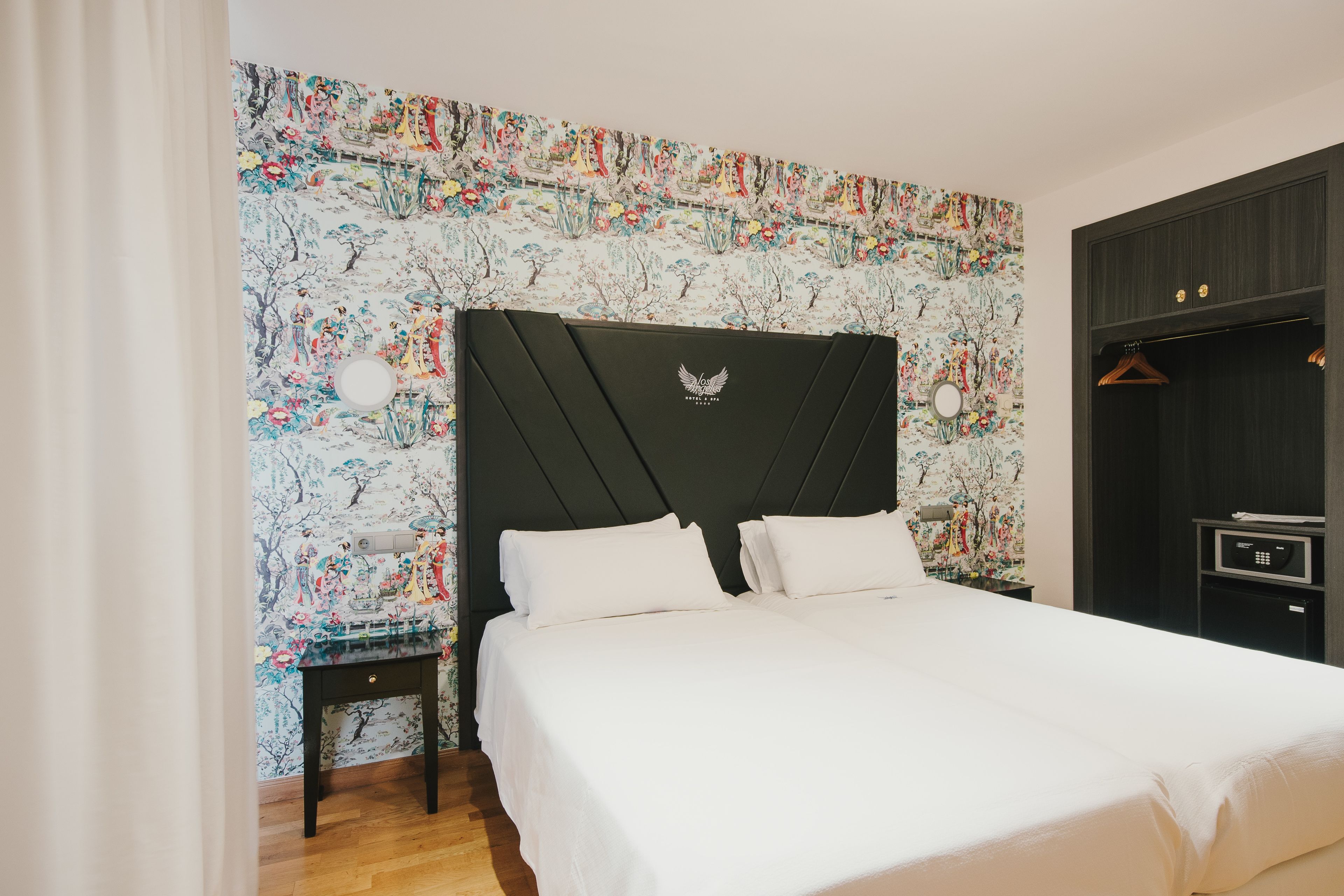 Ein Schlafzimmer mit einem großen Bett, einem Nachttisch, einem Kleiderschrank und einer Wand mit floralem Muster.