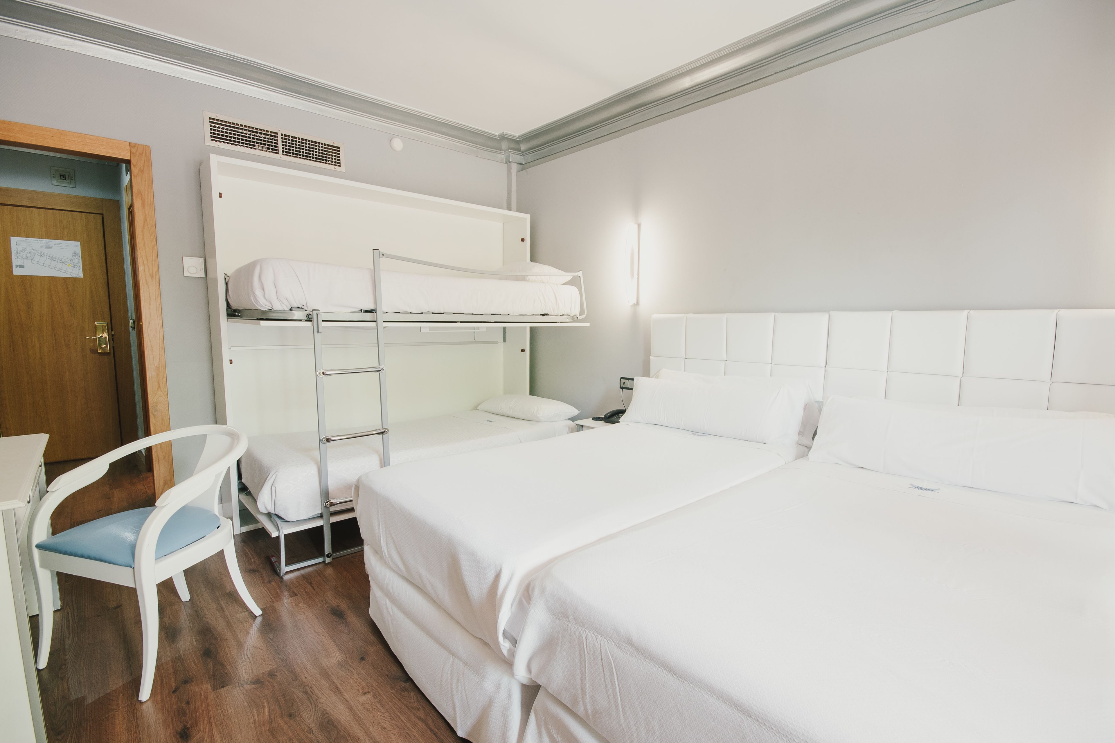 Habitación de hotel con literas, una cama individual, una silla y un escritorio.