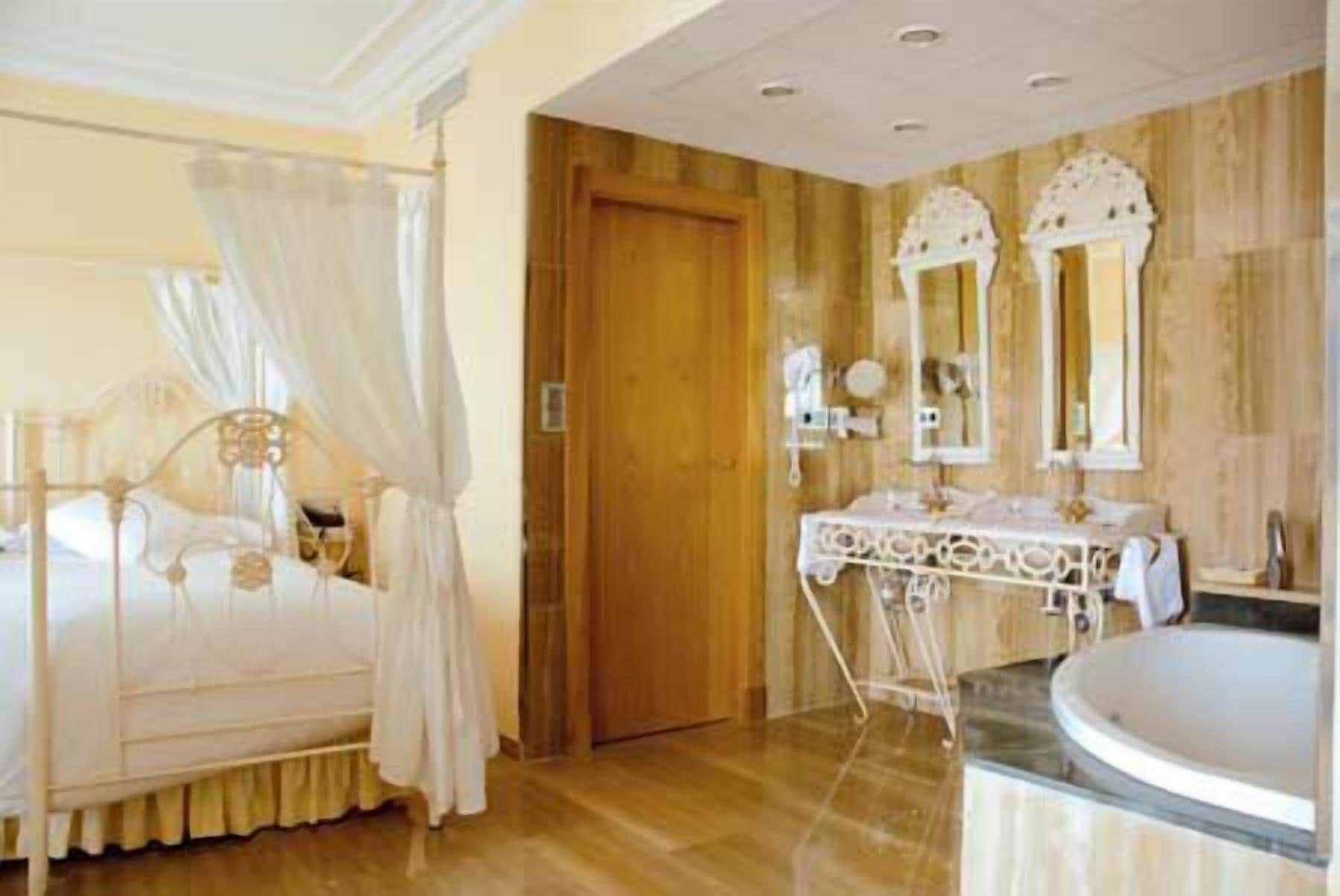 Un dormitorio con cama con dosel, una puerta de madera y un baño con lavabo y espejo.