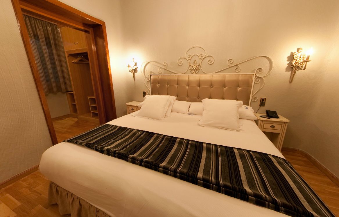 A neatly made bed with a striped bedspread, a wooden headboard, and two bedside tables with lamps.