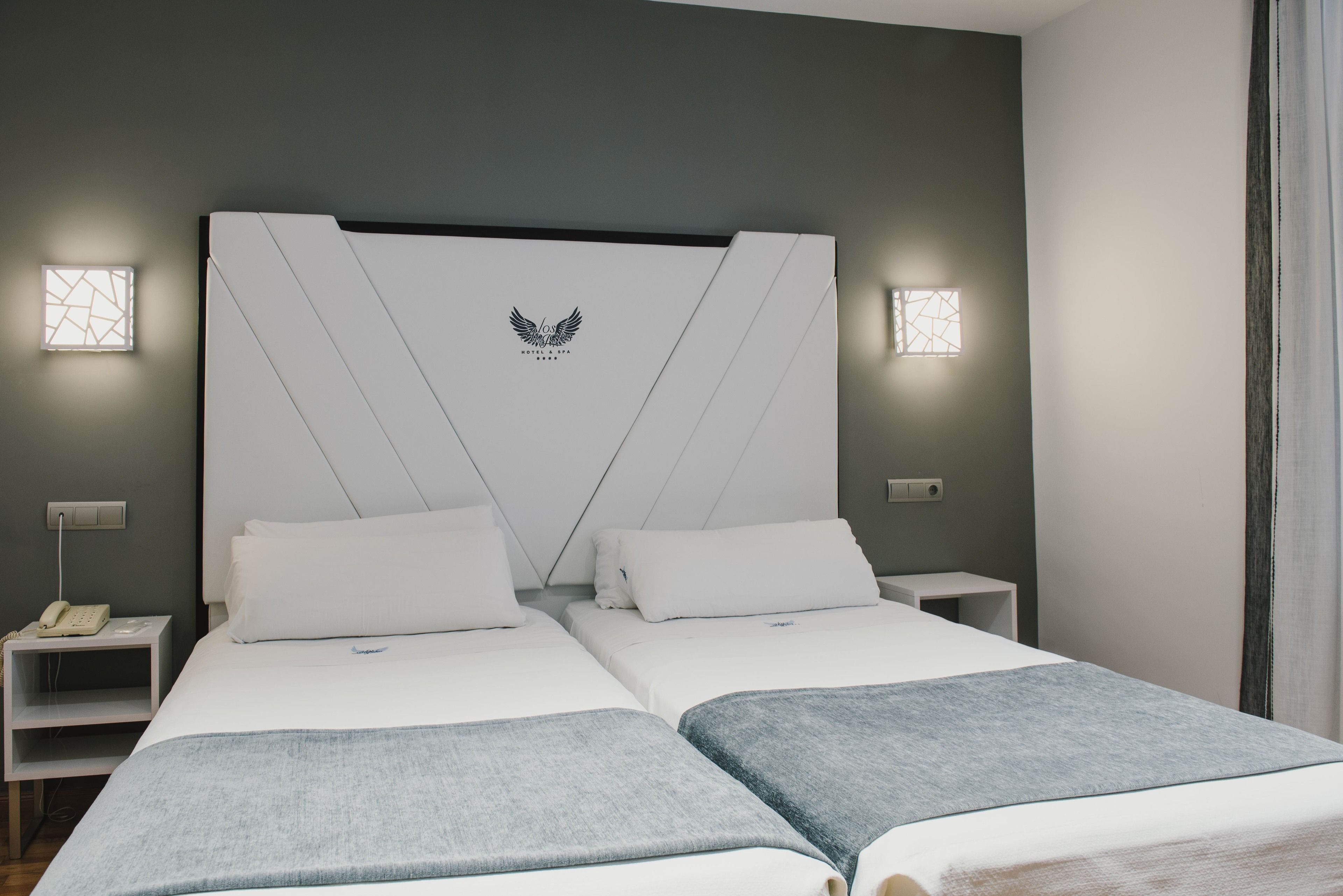A modern hotel room with a large bed, two bedside tables, and a headboard with a logo.