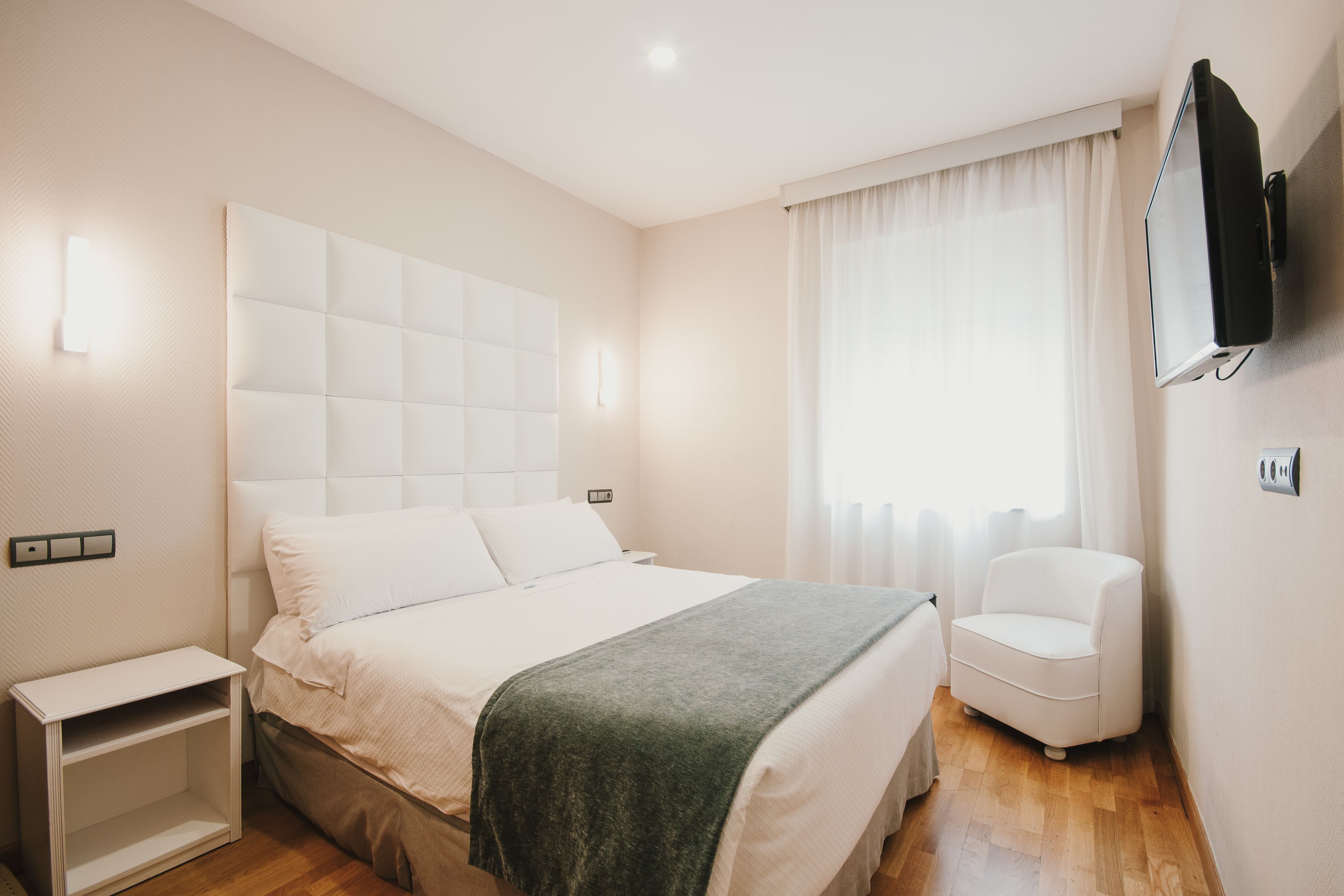 Une chambre bien rangée, avec un lit, une table de chevet, une chaise et un téléviseur fixé au mur.
