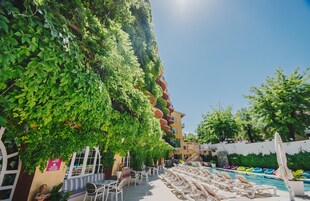 Ett område vid poolen med solstolar, en pool och en byggnad med en grön vägg täckt av växtlighet.