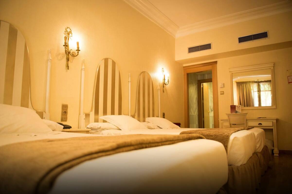 A hotel room with a large bed, bedside tables, a mirror, and a window with curtains.