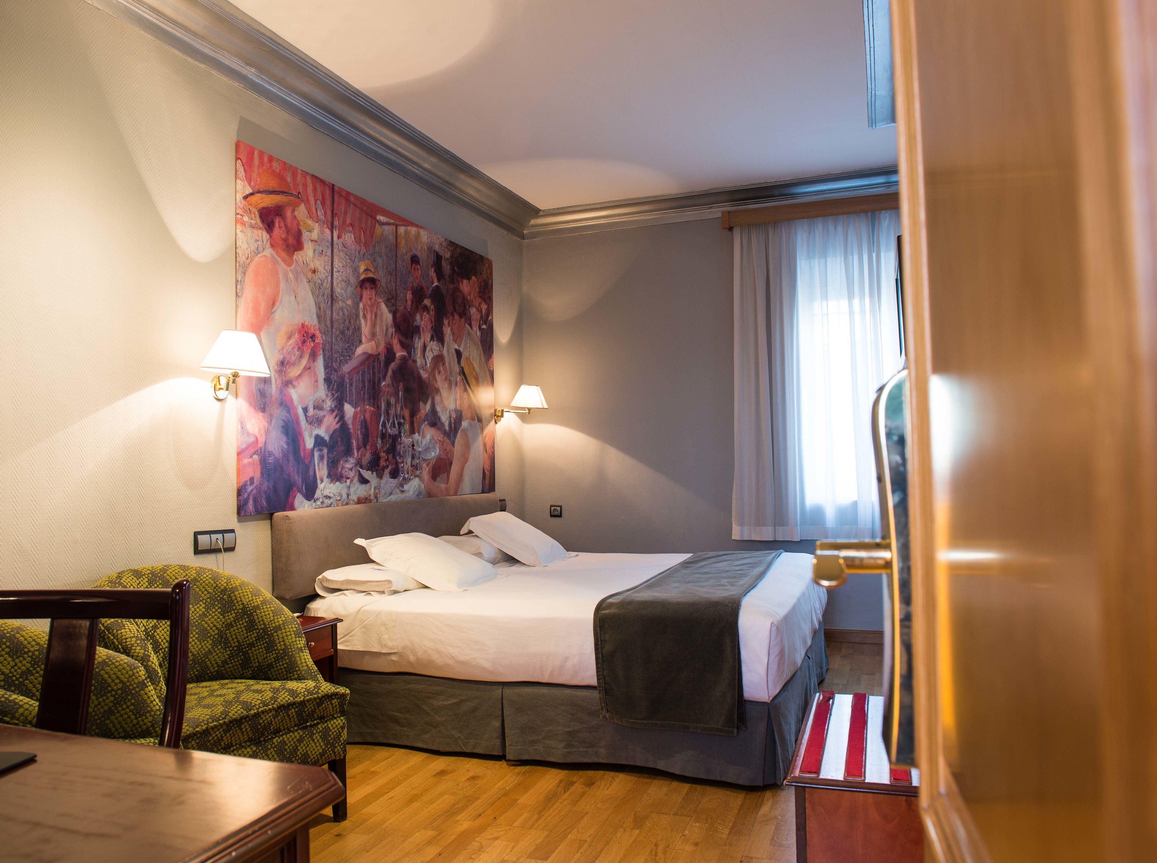Een hotelkamer met een bed, twee bedlampen, een schilderij aan de muur, een stoel en een raam met gordijnen.