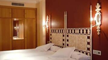 A hotel room with a double bed, wooden wardrobe, and decorative wall sconces.