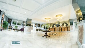 Un hallo amplio con mostrador de recepción, zona de estar y plantas decorativas.