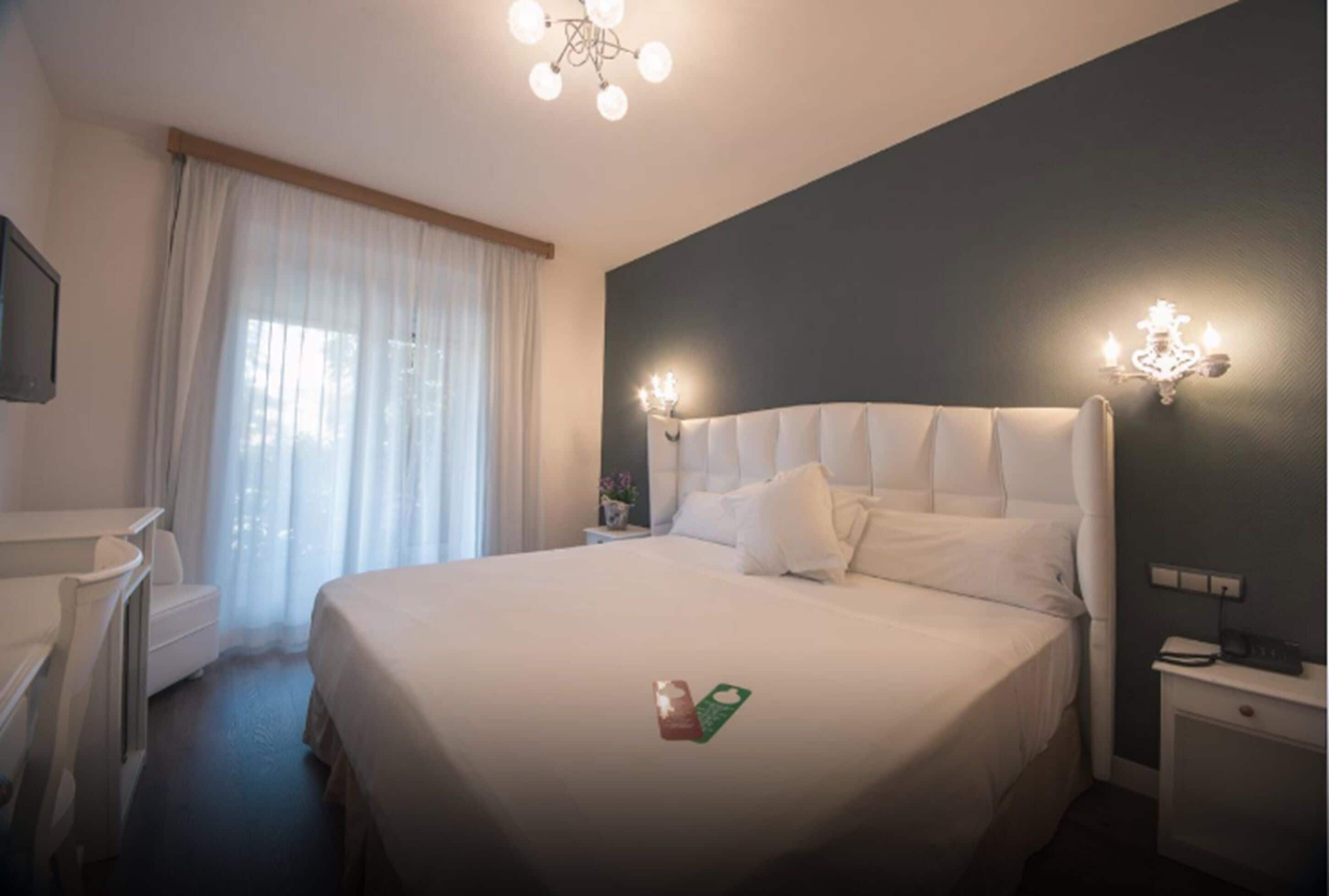 Una habitación de hotel con una cama grande, un escritorio y una silla. Cuenta con una ventana con cortinas, un candelabro y apliques de pared.