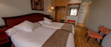 Habitación de hotel con una cama grande, cabecera de madera, un cuadro en la pared, un espejo y un rincón de descanso con dos sillones.