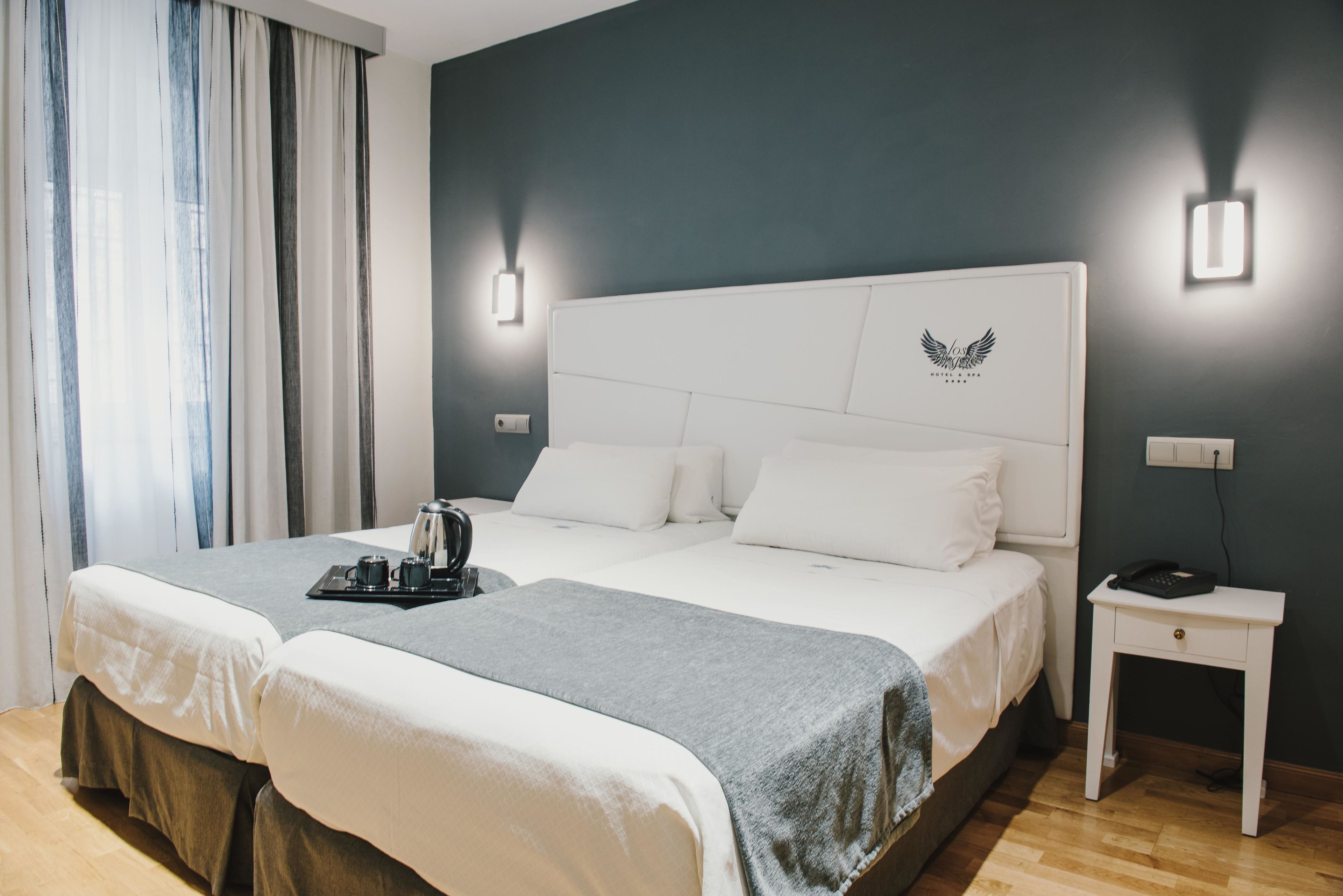 Una cama doble con colcha gris y blanca, dos mesitas de noche y una lámpara de pared.