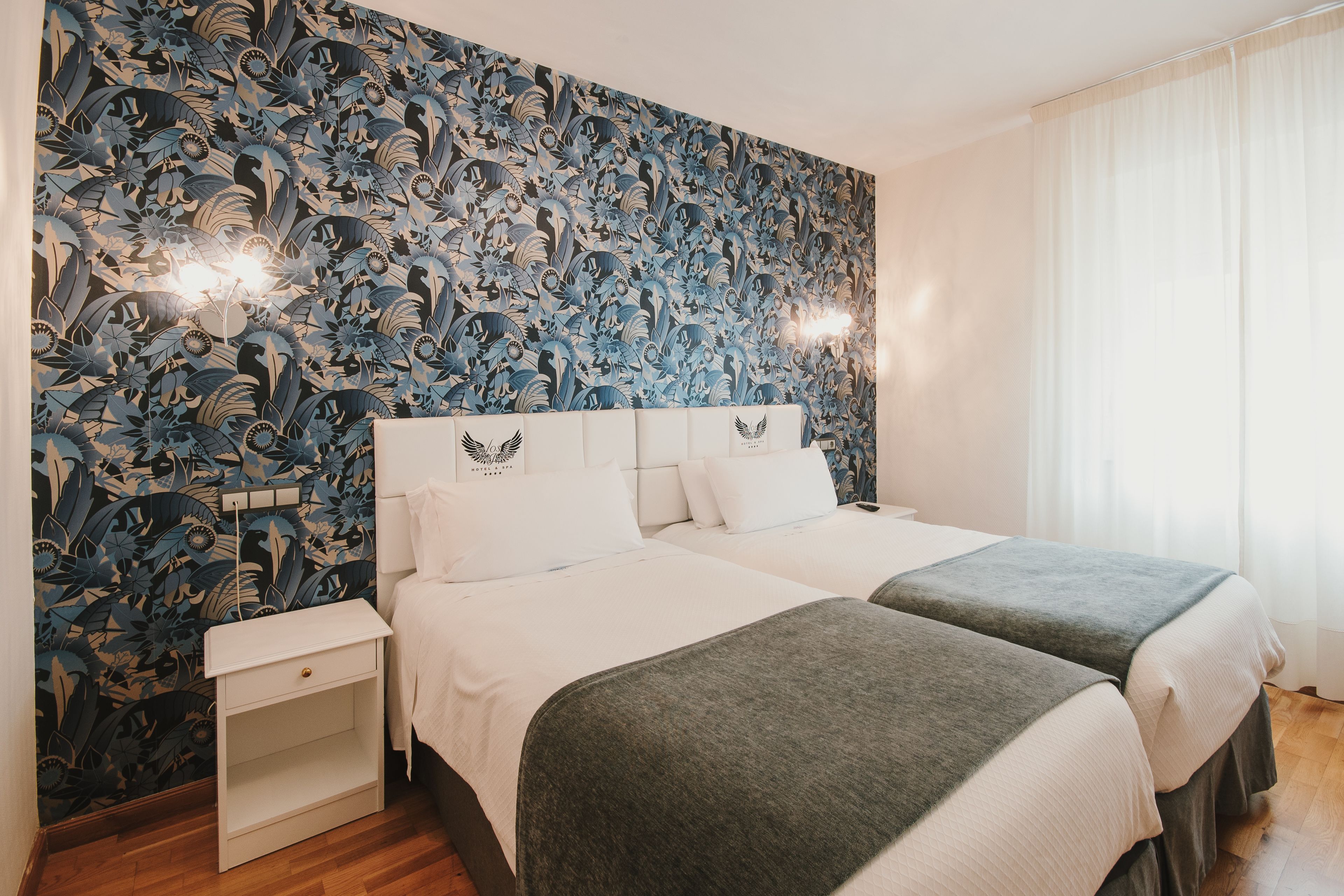 A hotel room with two beds, a nightstand, and a floral wallpaper.