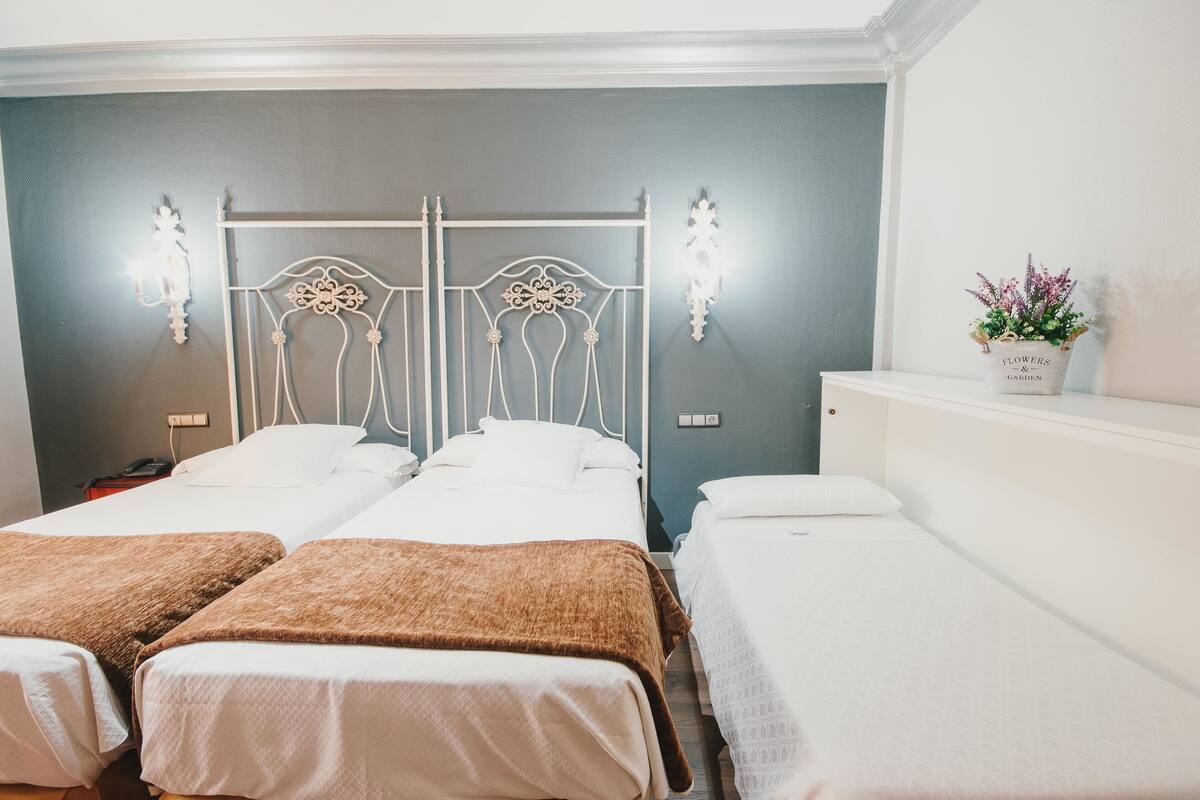 A hotel room with two beds, a white metal headboard, and a small potted plant on a nightstand.