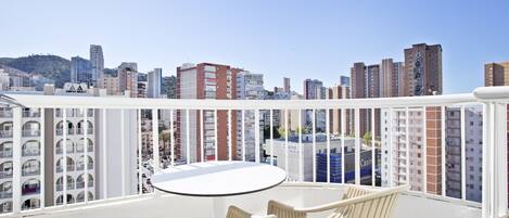 Un balcón con una mesa redonda y dos sillas, con vista a un paisaje urbano con varios edificios.