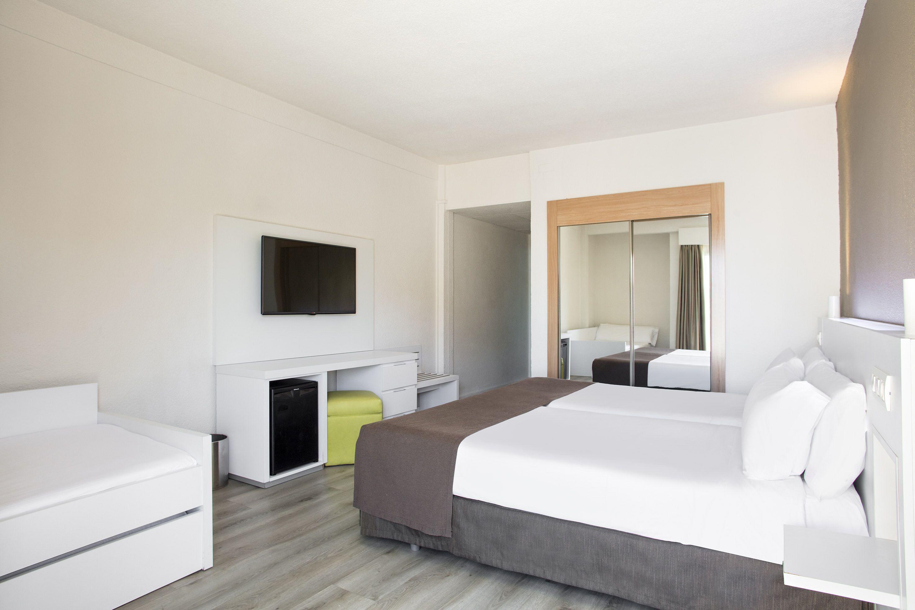 Una camera d'albergo moderna con un letto, una scrivania, una televisione e uno specchio.