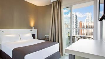 Habitación de hotel con cama, escritorio y balcón con vista a la ciudad.