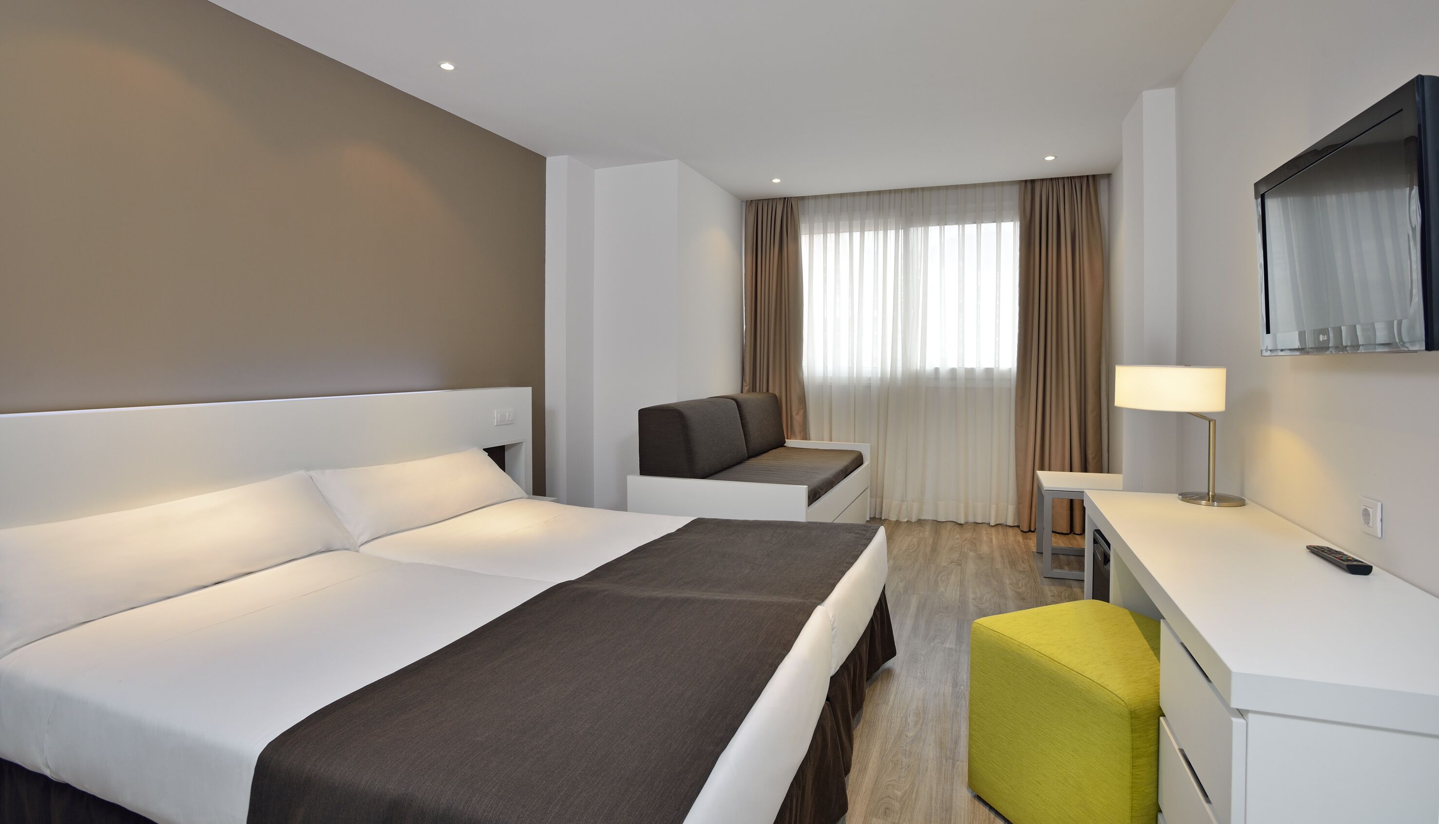 A hotel room with a bed, a sofa, a desk, and a TV.